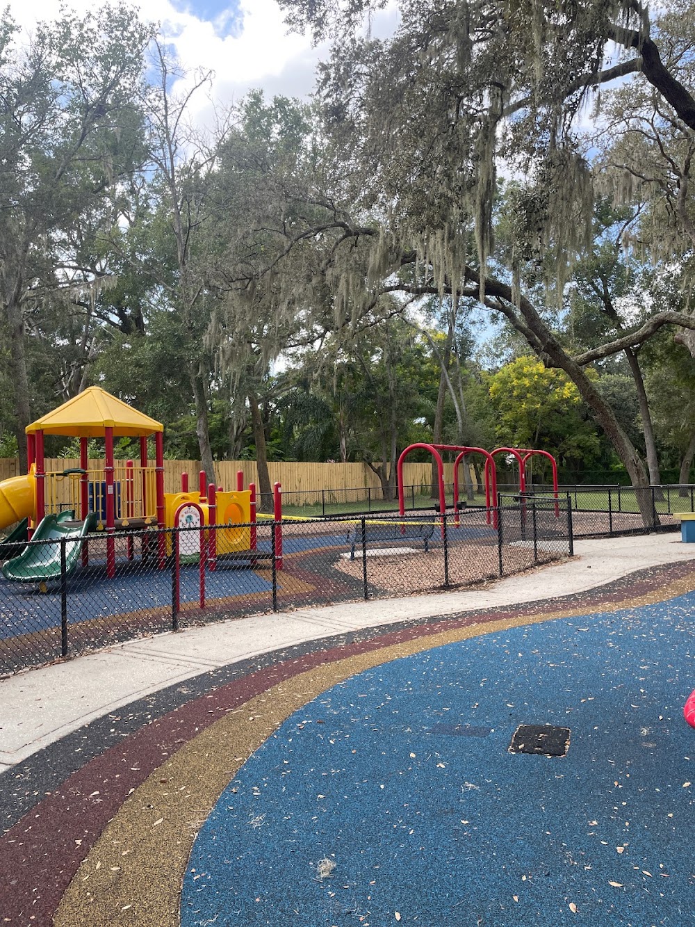Smaller fenced playground beneath large oak trees at All Person's Rotary Park